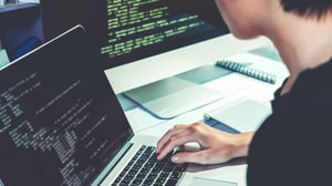 Computer programming at desk with computer screens